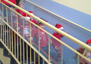 Dzieci schodzą po schodach do przedszkolnej szatni. Na głowie mają mikołajkowe czapki.