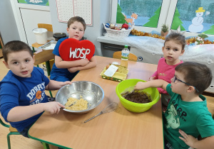 grupa dzieci przy stoliczku przygotowuje ciasteczka, na stole leżą składniki