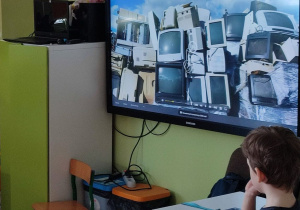 prezentacja na tablicy - slajd przedstawia górę zepsutych telewizorów, patrzy na to chłopiec