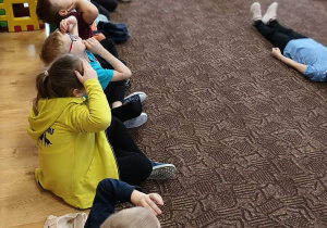 grupa dzieci siedzi w kole na dywanie, słucha prelekcji ratowniczki
