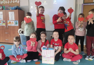 grupa dzieci ubranych na czerwono, trzymają w rączkach walentynki i pozują do zdjęcia