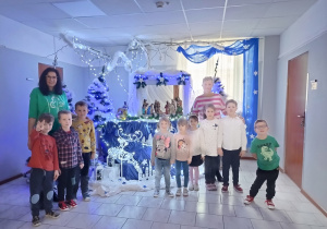grupa dzieci i nauczycielki pozują do zdjęcia na tle świątecznej dekoracji w DPS