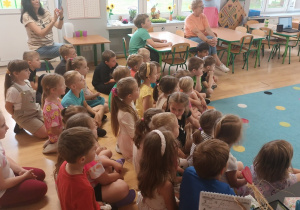 grupa dzieci siedzi na dywanie, obok nauczycielki, wszyscy oglądają występ p. "Spotkanie z folklorem"