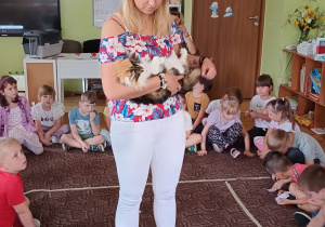 Przedstawicielka fundacji trzyma na rękach kota, wokoło , na dywanie siedzą dzieci