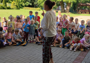 społeczność przedszkolna zebrana na tarasie (dzieci, pracownicy), słuchają bajkę czytaną przez nauczycielki