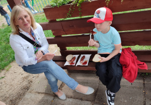 kobieta i dziecko w przedszkolnej altanie, chłopiec je kiełbaski z grilla