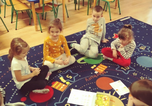 Dzieci siedzą na dywanie i grają w grę "kurnik"