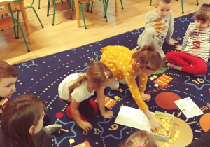 Dzieci siedzą na dywanie i grają w grę "kurnik"