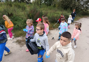 grupa dzieci na polnej drodze, mająna rękach jednorazowe rękawiczki, niektóre trzymają "łapaki", zbierają śmieci