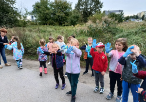 grupa dzieci na polnej drodze, mająna rękach jednorazowe rękawiczki, niektóre trzymają "łapaki",
