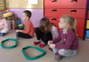 czworo dzieci siedzi na dywanie, wykonują zadanie matematyczne