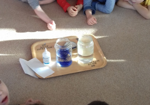dzieci leżą na dywanie i obserwują eksperyment z wodą i atramentem
