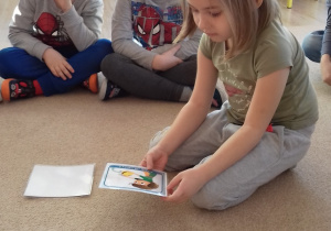 dziecko siedzi na dywanie i opisuje co widzi na obrazkach
