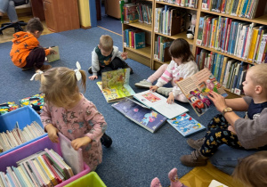 dzieci siedzą na dywanie w bibliotece, oglądają ksiażeczki