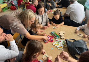 rodzice z dziećmi siedzą przy stolikach, wspólnie wykonują ozdoby świąteczne