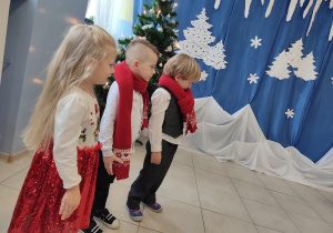 troje dzieci na "scenie", są odświętnie ubrane , na szyjach czerwone szaliki