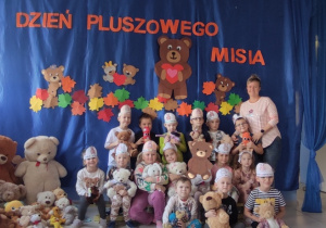 grupa dzieci pozuje do wspólnego zdjęcia, obok stoi nauczycielka, dzieci trzymają pluszowe misie, na głowach mają opaski z misiami