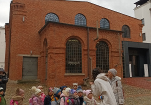 grupa dzieci i nauczycielka stoją przed muzeum , słuchają pani przewodniczki