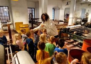 grupa dzieci i ich panie w muzeum, słuchają pani przewodniczki , oglądają maszyny włókiennicze