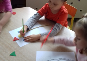 chłopiec siedzi przy stole i odrysowuje na kartce figury geometryczne