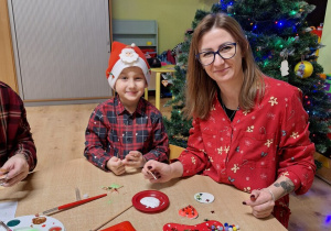 Mama z synem pozują do zdjęcia podczas przygotowania ozdób choinkowych.