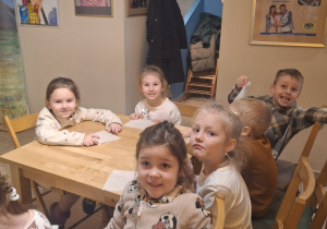 Dzieci siedzą przy stoliku, czekają na rozpoczęcie przedstawienia. Pozują do zdjęcia.
