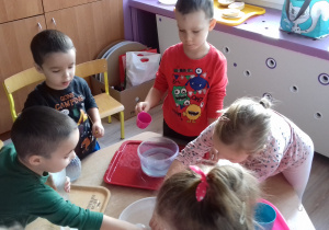 dzieci stoją przy stoliku i przelewają wodę w różnych naczyń