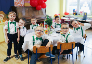 Grupa chłopców pozuje do zdjęcia. Wszyscy ubrani są w białe koszule, eleganckie spodnie, zielone muchy i szelki.