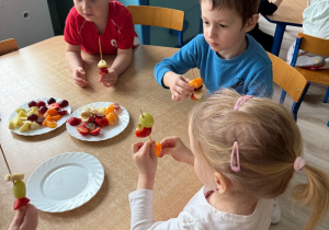 troje dzieci wykonuje szaszłyki z owoców