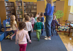 grupa dzieci chodzi między szafkami w bibliotece , obok pani bibliotekarka