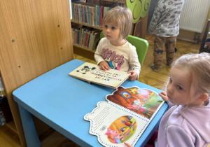 dwoje dzieci siedzi przy stoliku, oglądają książeczki