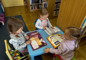 grupa dzieci siedzi przy stoliku, oglądają książeczki