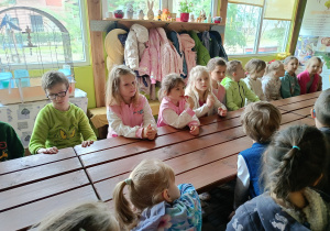grupa dzieci w pomieszczeniu, siedzą przy długim stole, biorą udział w warsztatach o pszczołach