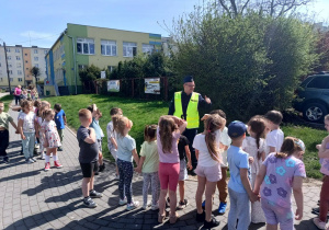grupa dzieci przygotowuje się do przejścia po pasach, obok stoi policjant