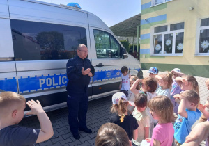 grupa dzieci przy radiowozie, słuchają policjanta