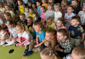 grupa dzieci siedzi na dywanie, oglądają przedstawienie , żywo reagują