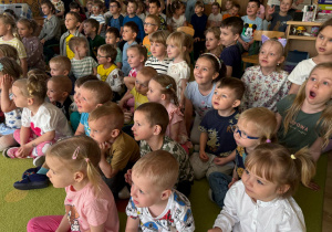grupa dzieci siedzi na dywanie, oglądają przedstawienie , żywo reagują