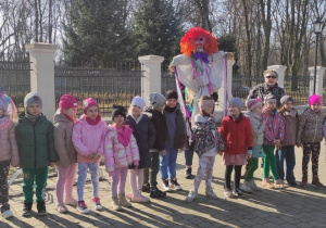 grupa dzieci i nauczycielki na dziedzińcu MOK, nauczycielka trzyma marzannę