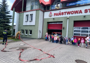 grupa dzieci przy jednostce PSP, patrzą, jak strażacy podłączają wąż do hydrantu