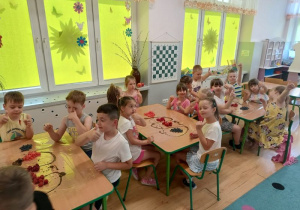 dzieci przy stolikach jedzą owoce