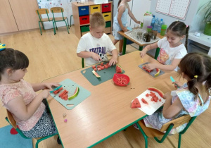 dzieci siedzą przy stoliku, kroją owoce