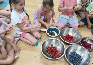dzieci siedzą na podłodze wokół misek z owocami
