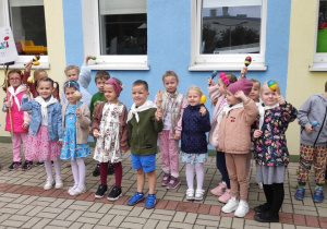 grupa przedszkolaków przed budynkiem przedszkola, w rękach trzymajągrzechotki