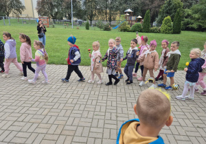 grupa przedszkolaków podczas zabawy kołowej w przedszkolnym ogrodzie , niektóre dzieci mają w rączkach grzechotki