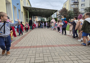 grupa dzieci i ich panie podczas zabawy muzycznej w ogrodzie przedszkolnym