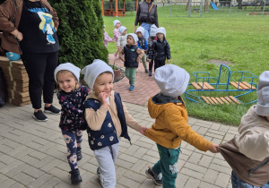 maluszki stojąw rzędzie, obok ich panie , dzieci mają na głowach czapki smerfetki