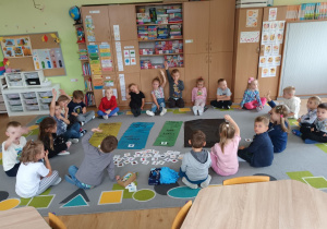Dzieci siedzą na dywanie w trakcie zajęć dydaktycznych. Na dywanie znajdują się kolorowe worki na odpady.