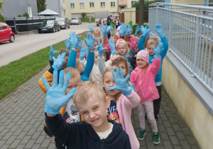 Dzieci pozują do zdjęcia. Unoszą ręce i prezentują niebieskie rękawiczki ochronne.