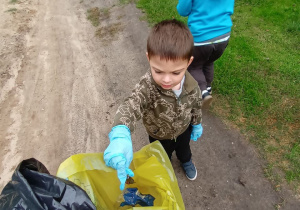 Chłopiec wrzuca papierek do żółtego worka. W tle znajduje się grupa dzieci.