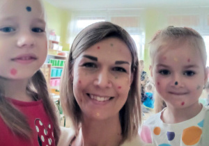 Nauczycielka i dwie dziewczynki pozują do zdjęcia. Na twarzach mają namalowane kolorowe kropki.